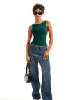 Woman in green one-shoulder top, wide-leg jeans, sunglasses, and white sneakers holding black bag