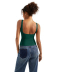 Woman wearing green backless tank top with wide straps, paired with blue jeans, showcasing casual women's clothing style.