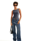 Woman in gray one-shoulder bodysuit with wide-leg jeans, sunglasses, and white sneakers