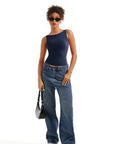 Woman in navy one-shoulder top, wide-leg jeans, sunglasses, and white sneakers holding black bag