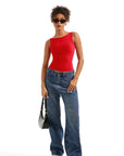 Woman in red one-shoulder top, wide-leg jeans, sunglasses, and white sneakers holding black bag
